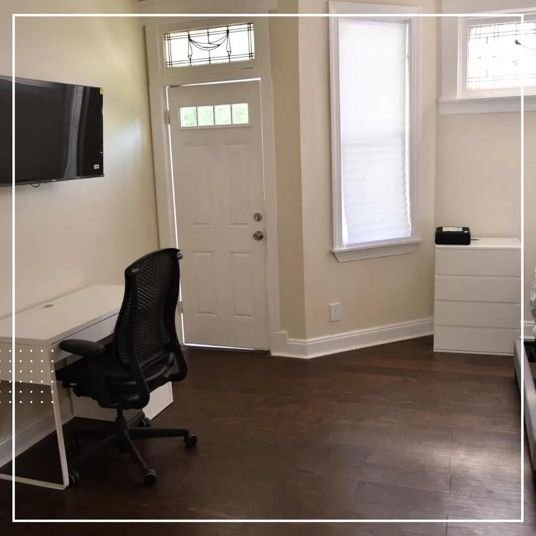 Furnished room with a wall-mounted TV, desk and chair, and dresser